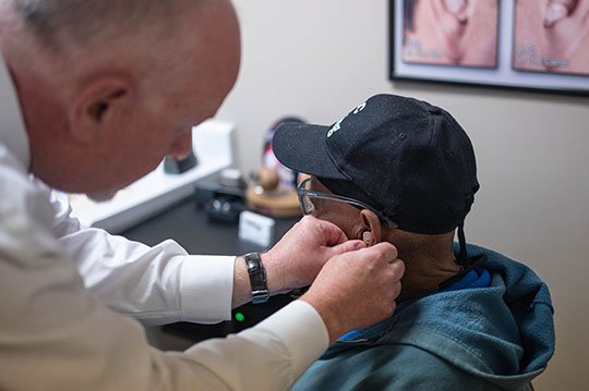 An audiologist fits a patient with a hearing aid.