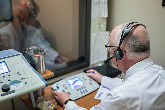 An audiologist testing a patient's hearing in a hearing booth